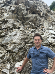 Adam Curry poses, leaning against a rock wall.
